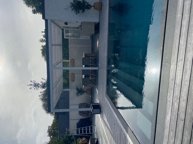 Rektangulär pool med grått trädäck, vit pergola och utekök – komplett poolmiljö