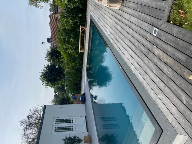 Nyinstallerad modern pool med grått trädäck, overflow-kant och vitt poolhus – ett av våra projekt i Mälardalen