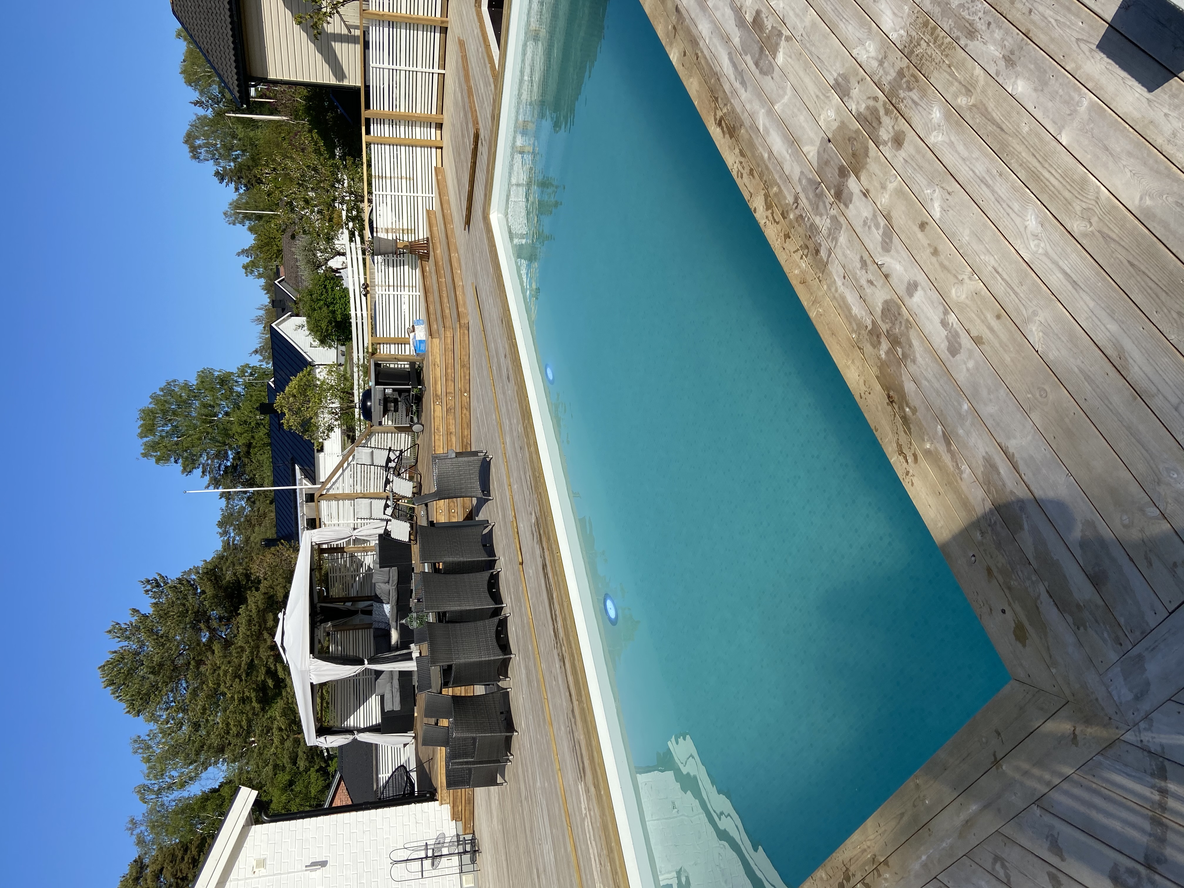 Rektangulär pool med grått trädäck, pergola och utemöbler – ett av våra genomförda projekt