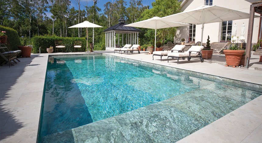 Stor lyxpool med granit- och marmorplattor, solstolar och lyxig poolmiljö